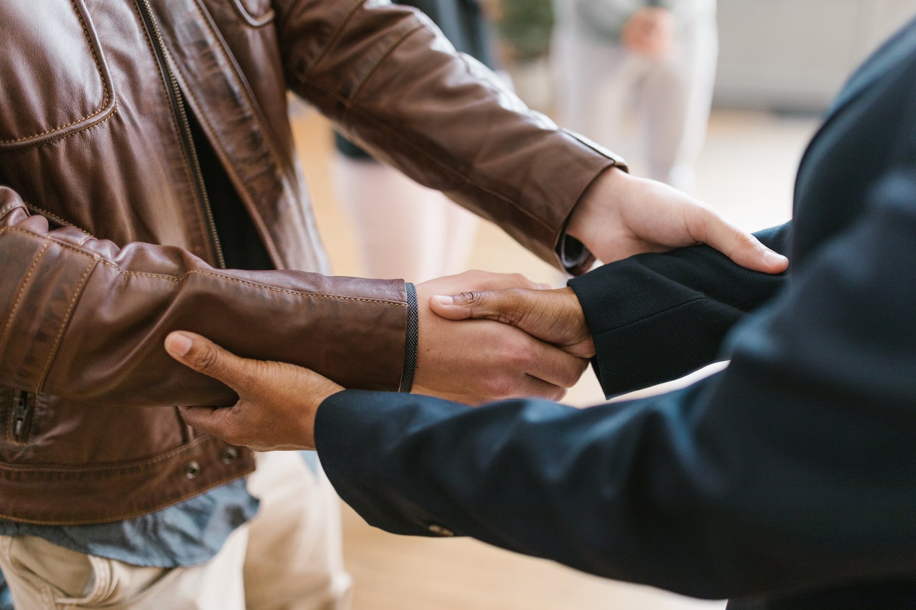 person in black suit shaking hand with a person in brown leather jacket